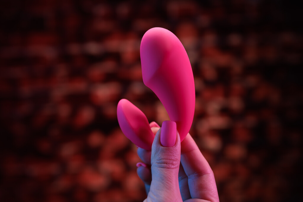 Hand holding a Pink clitoral vibrator for women with a sparkle background